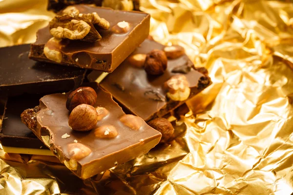 Close-up, verschillende soorten chocoladestukjes en hazelnoten. verscheidenheid van chocolade op gouden folie verpakking — Stockfoto