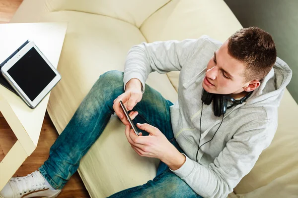 Man on couch with headphones smartphone and tablet — Stock Photo, Image