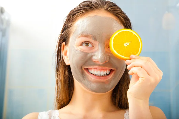 Vrouw met modder gezichtsmasker houdt oranje plak — Stockfoto