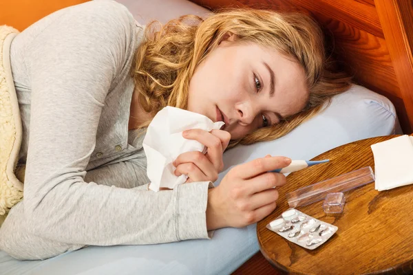 Mujer enferma en la cama con termómetro y pastillas . — Foto de Stock