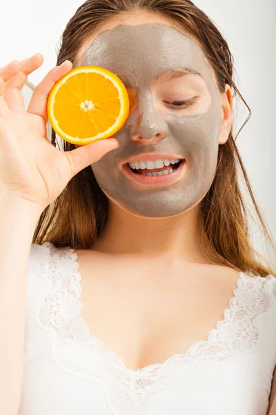 Kvinna med lera ansiktsmask håller orange skiva — Stockfoto