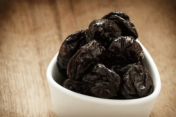 Dried plums prunes in white bowl on wooden table — Stock Photo, Image