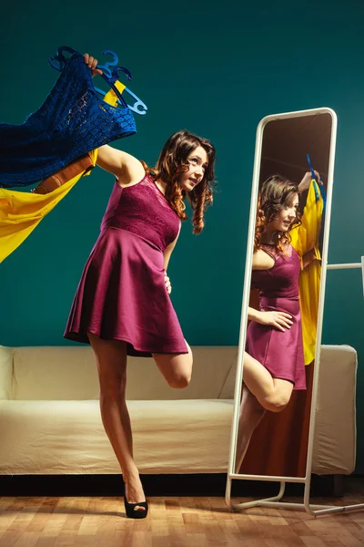 Mujer comprador sostiene perchas con ropa mirando en el espejo — Foto de Stock