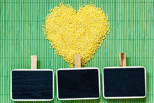 Millet groats heart shaped on green mat surface. — Stock Photo, Image