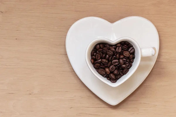 Pohár s kávová zrna na dřevěný stůl ve tvaru srdce — Stock fotografie