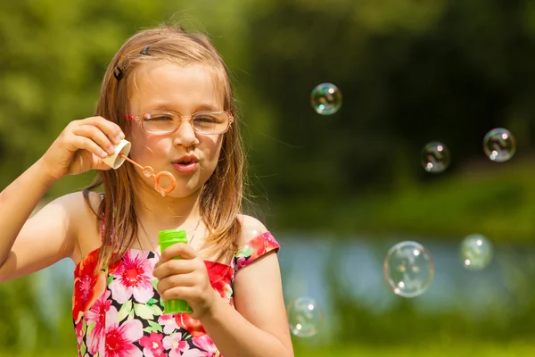 Lilla flickan barnet blåser såpbubblor utomhus. — Stockfoto