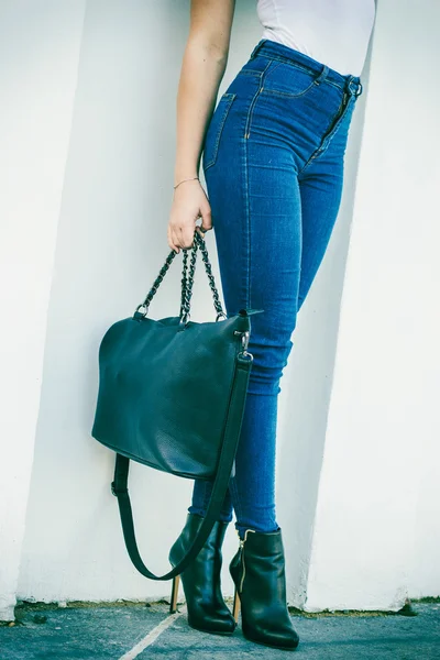 De benen van de vrouw in hakken schoenen handtas in de hand — Stockfoto