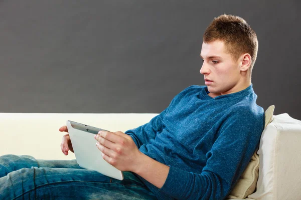 Joven con la tableta sentado en el sofá en casa — Foto de Stock