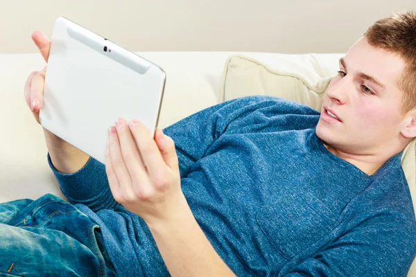 Jovem com tablet digital deitado no sofá — Fotografia de Stock