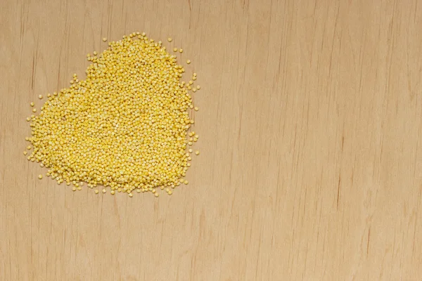 Millet groats heart shaped on wooden surface. — Stock Photo, Image