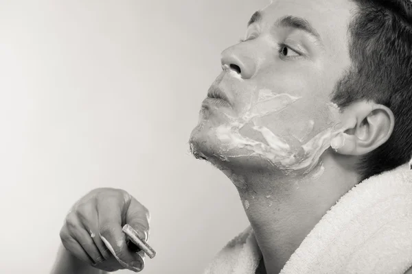 Jeune homme rasage à l'aide d'un rasoir avec mousse crème . — Photo