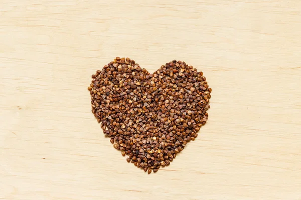 Trigo sarraceno grumos coração moldado na superfície de madeira. — Fotografia de Stock