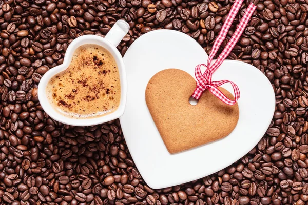 Чашка в форме сердца и печенье на фоне кофейных зерен — стоковое фото