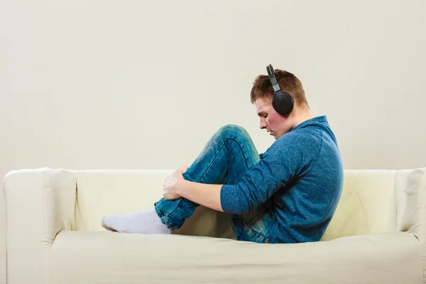 Muž se sluchátky na uších sedí na gauči — Stock fotografie