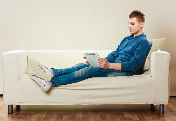 Mladý muž s tabletou sedí doma na gauči — Stock fotografie