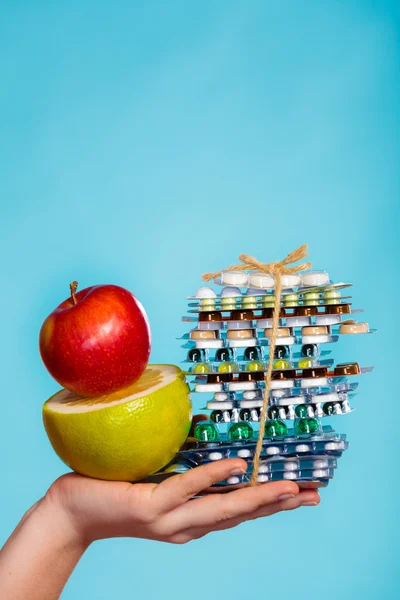 Lidská ruka držící stack pilulek a ovoce na modré. — Stock fotografie