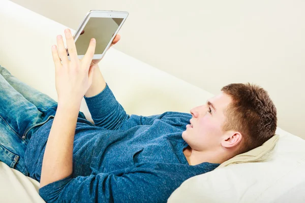 Jovem com tablet digital deitado no sofá — Fotografia de Stock