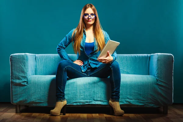 Kobieta z tabletką siedzi na kanapie niebieski kolor — Zdjęcie stockowe
