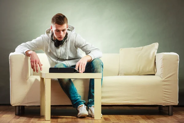 Uomo con cuffie seduto sul divano con tablet — Foto Stock