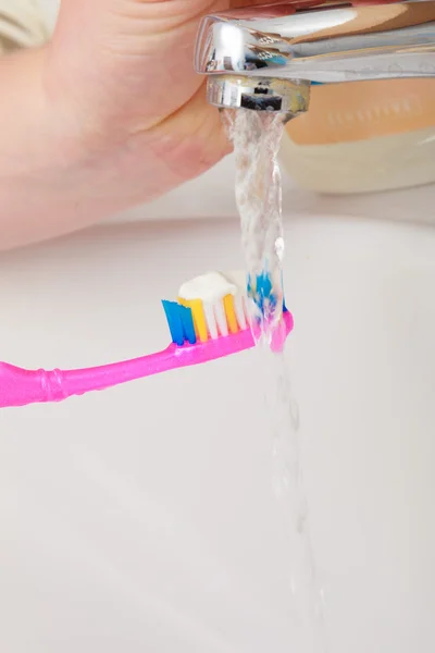 Pasta de dientes en el cepillo de dientes en la mano, en el lavabo del baño . — Foto de Stock