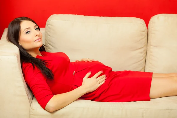 Schwangere entspannt sich auf Sofa und berührt ihren Bauch — Stockfoto