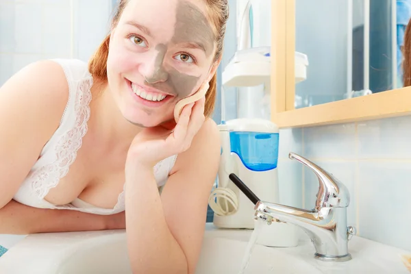 Woman removing facial clay mud mask in bathroom — Stock Photo, Image