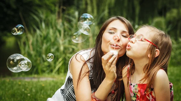 Mother and little girl blowing soap bubbles in park. — Stock Photo, Image