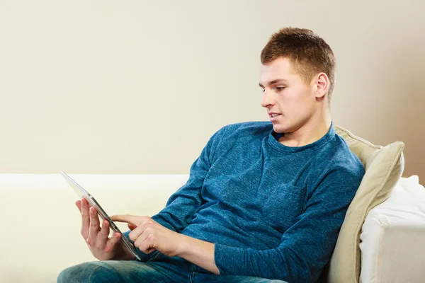 Jovem com tablet sentado no sofá em casa — Fotografia de Stock