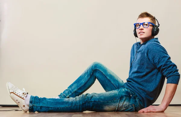 Giovane uomo con le cuffie seduto sul pavimento — Foto Stock
