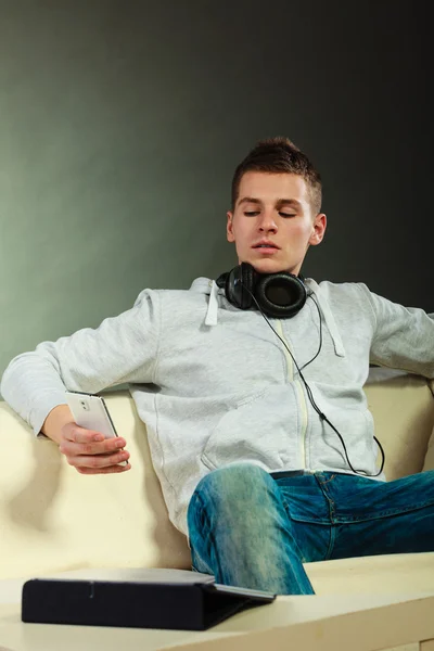 Homem no sofá com fones de ouvido smartphone e tablet — Fotografia de Stock