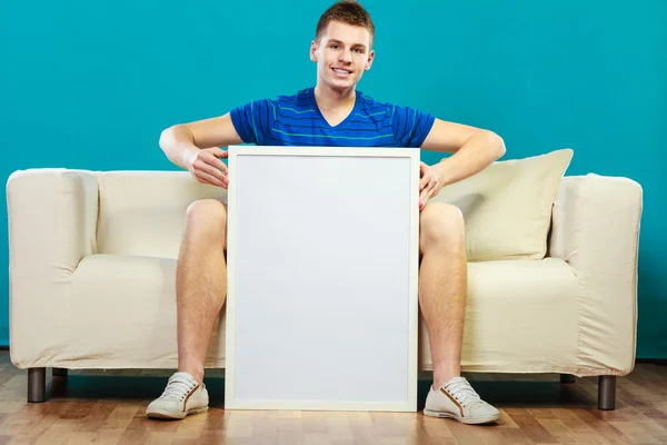 Man on sofa holding blank presentation board — Stock Photo, Image