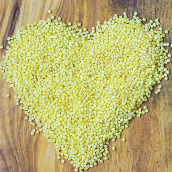 Millet groats heart shaped on wooden surface. — Stock Photo, Image