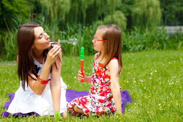 Мать и девочка пускают мыльные пузыри в парке . — стоковое фото