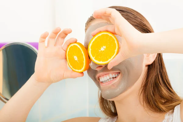 Γυναίκα με μάσκα προσώπου λάσπη κρατά φέτα πορτοκάλι — Φωτογραφία Αρχείου