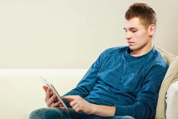 Mladý muž s digitálním tabletu sedí na gauči — Stock fotografie