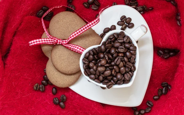 Coffee beans in heart shaped cup and dessert on red — Stock Photo, Image