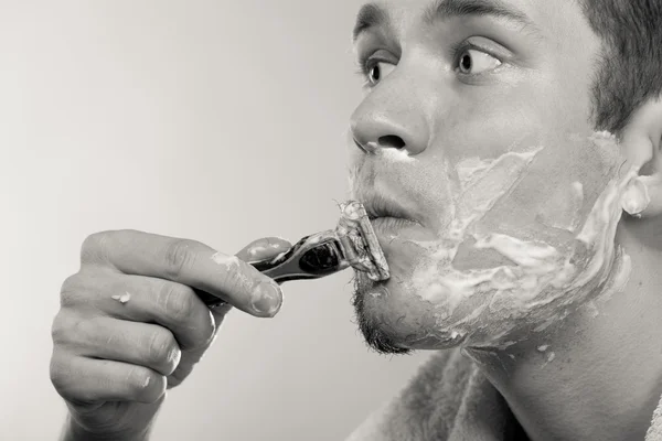 Jeune homme rasage à l'aide d'un rasoir avec mousse crème . — Photo