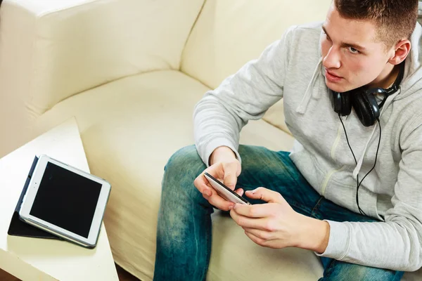 Hombre en el sofá con auriculares smartphone y tableta —  Fotos de Stock