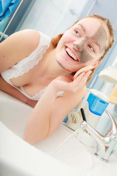 Woman removing facial clay mud mask in bathroom — Stock Photo, Image