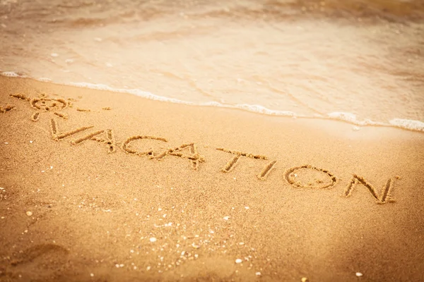 A word nyaralás írt a homok a tengerparton — Stock Fotó