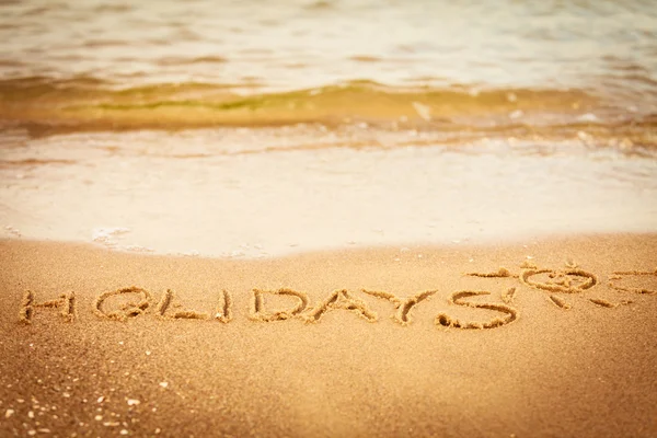 Le mot vacances écrit dans le sable sur une plage — Photo