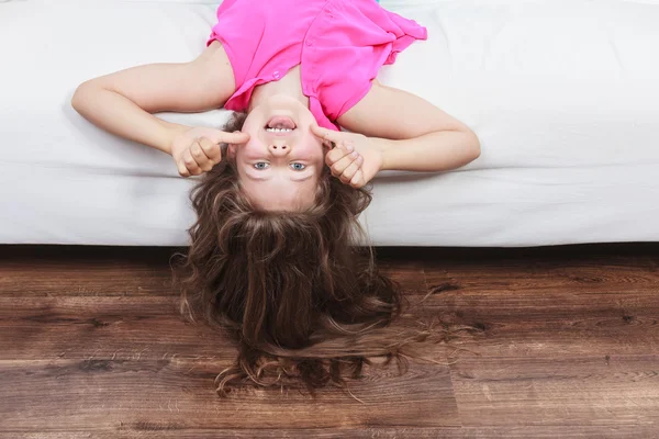 Malá dívka s dlouhými vlasy vzhůru nohama na gauči — Stock fotografie