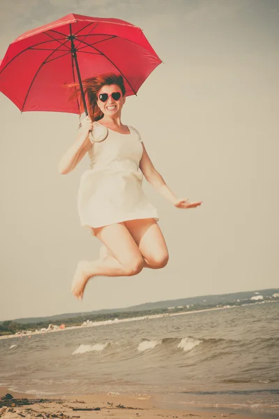 Mädchen springt mit rotem Regenschirm am Strand. — Stockfoto