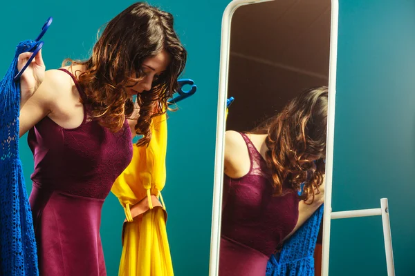 Γυναίκα αγοραστής κρατά κρεμάστρες με ρούχα κοιτάζοντας στον καθρέφτη — Φωτογραφία Αρχείου