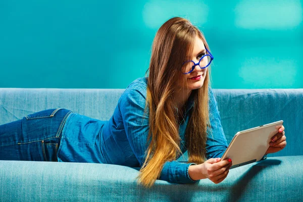 Женщина с планшетным отдыхом на диване голубого цвета — стоковое фото