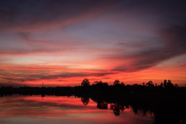 Kırmızı turuncu gökyüzü ile gölün üzerinde gün batımı.