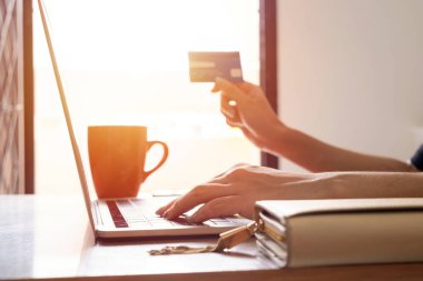 Kredi kartı tutan ve dizüstü bilgisayar kullanan eller. İnternetten alışveriş