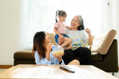 Üç yaş aralığı, Asyalı yeğen ve büyükanne film izlemekten ve evdeki oturma odasında patlamış mısır yemekten zevk alıyorlar.