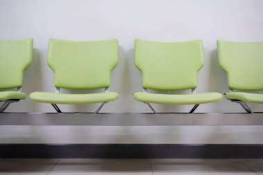 Row of green office chairs standing in corridor or conference room, empty dark seats arranged in line in boardroom, range of basic stools in front of white wall. Interview, recruitment concept