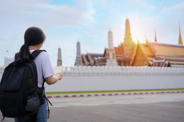 Asian girls look at a map about Wat Phra Kaew to travel in the Grand Palace in Bangkok, Thailand.